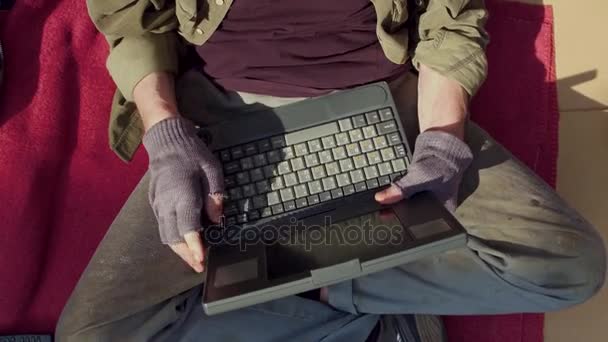 Nahaufnahme eines Obdachlosen, der auf Pappe sitzt und auf Laptop tippt. — Stockvideo