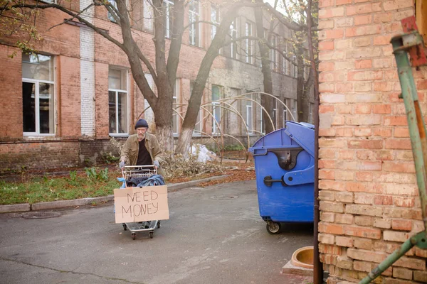 Mendicante senzatetto con carrello della spesa rubato con vitto bisogno di soldi su di esso . — Foto Stock