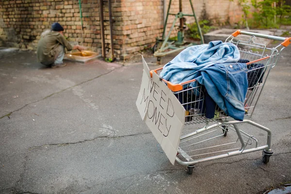 On front view shopping cart with belongings oh tramp, old man washing hands on backdrop. — Stock Photo, Image