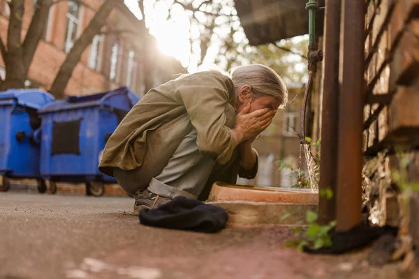 Pouliční život, bezdomovec squating umýt obličej. — Stock fotografie