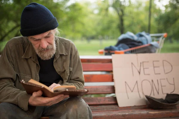 Old beardy man with no home reading a book. — Stock Photo, Image