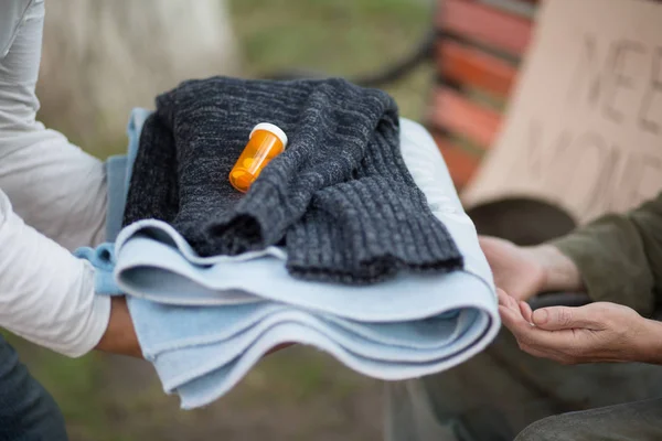 Vista de cerca de las manos con toalla de ropa de abrigo y medicina para hombre sin hogar . —  Fotos de Stock