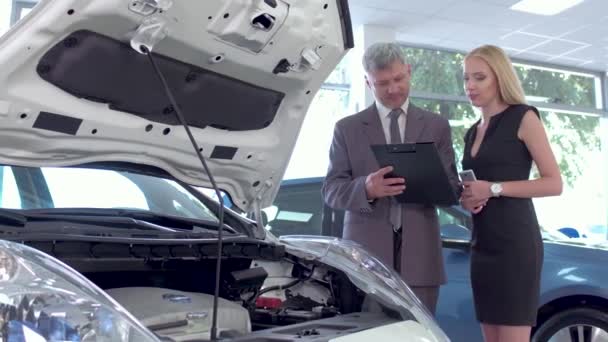 Dealer showing electric car to young woman in auto salon. — Stock Video