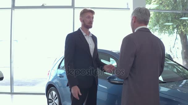 Young man at auto showroom talking with vehicle dealer. — Stock Video