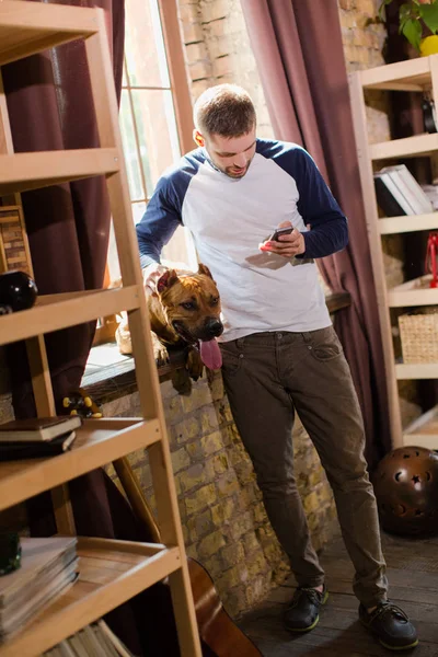 Hombre con ropa casual de pie junto a la ventana mirando el teléfono inteligente . — Foto de Stock