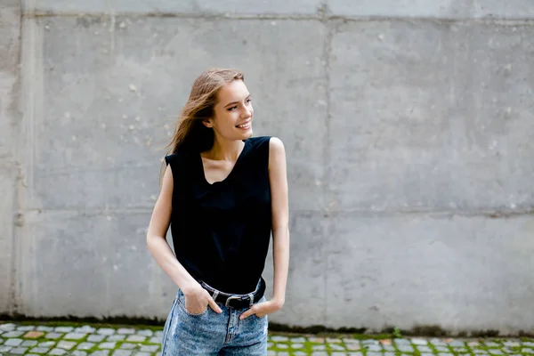 Blick auf hübsche junge Frau, die auf der Straße gegen graue Wand steht — Stockfoto