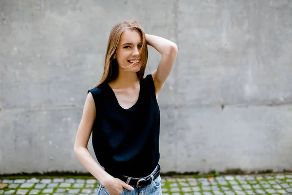 Attraktive lächelnde junge Frau, die auf der Straße steht und mit einer Hand den Kopf berührt. — Stockfoto