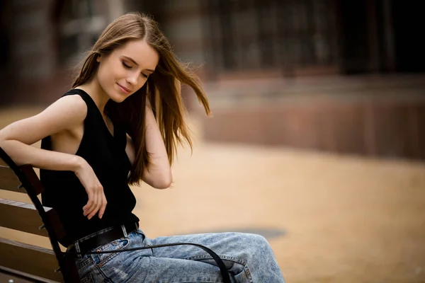 Sensual young woman touching her hair while sitting on bench. — Stock Photo, Image