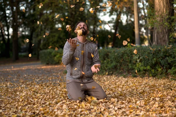 Άνθρωπος στον αθλητισμό φθορά παίζοντας με αποξηραμένα φύλλα στο πάρκο. — Φωτογραφία Αρχείου