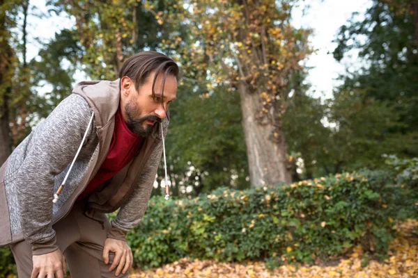 Man having short rest to take a breath after running in urban park.