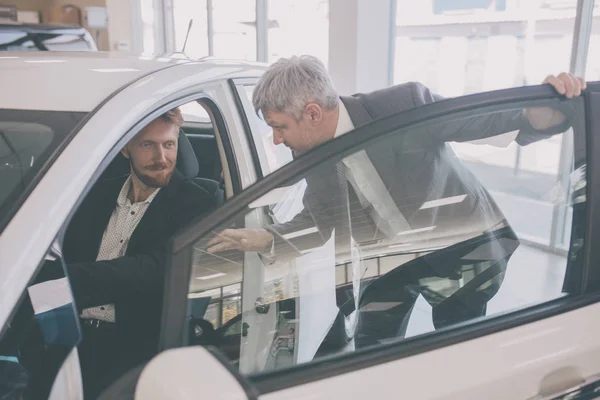 Concesionario de vehículos mostrando coche nuevo a joven hombre guapo . —  Fotos de Stock