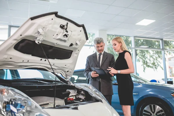 Auto dealer showing motor of electric car to young woman. — Stock Photo, Image