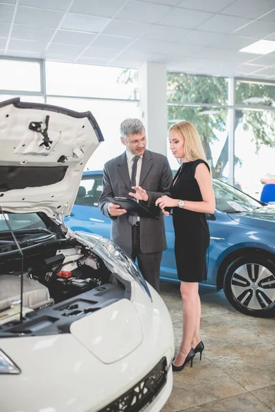 Auto showroom, young woman choosing car talking to dealer. — Stock Photo, Image