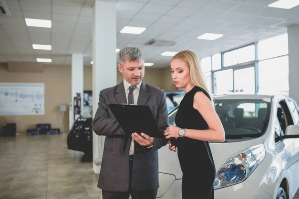 Concesionario de vehículos y mujer joven en sala de exposición de automóviles . —  Fotos de Stock