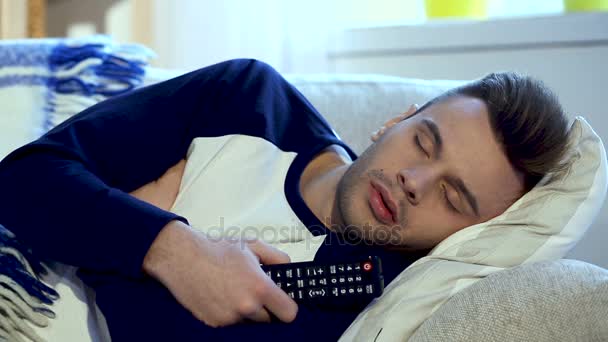 Homem dormindo no sofá com TV remota em suas mãos . — Vídeo de Stock