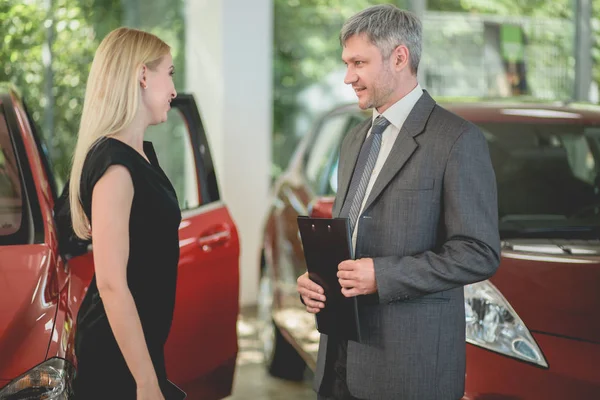 Vehicle dealer selling electric car to young pretty woman. — Stock Photo, Image