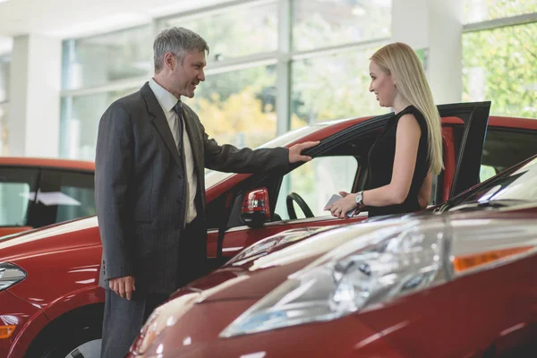 Auto showroom, young woman choosing car talking to dealer. — Stock Photo, Image