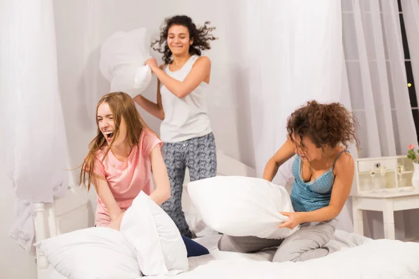 Chicas en la cama teniendo pelea de almohadas en pijama —  Fotos de Stock