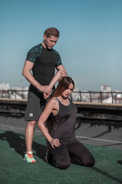Fitness op het dak, jonge vrouw, die zich uitstrekt met personal trainer. — Stockfoto