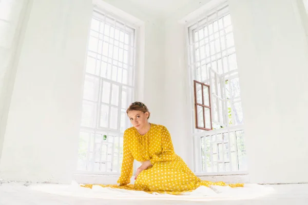 Женщина в жёлтом платье в горошек на полу в большой комнате — стоковое фото