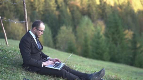 Um trabalhador de escritório está digitando algo em seu laptop nas montanhas — Vídeo de Stock