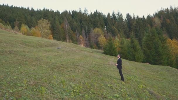 Een man van middelbare leeftijd in een pak klom een berg op om een video te maken met een drone. — Stockvideo