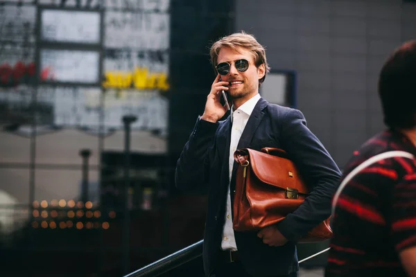 Ofiste çalışan orta yaşlı bir adam sokakta elinde bir çantayla yürüyor ve cep telefonuyla gülümsüyor. — Stok fotoğraf
