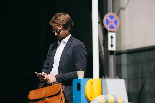 Podnikatel v obleku stojí na parkovišti Čtení novinek na mobilním telefonu — Stock fotografie