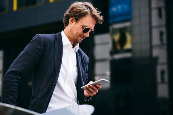 잘생긴 매력적 인 사무직원 이 선글라스를 끼고 거리에서 서 자신의 휴대 전화를 보고 있습니다. — 스톡 사진