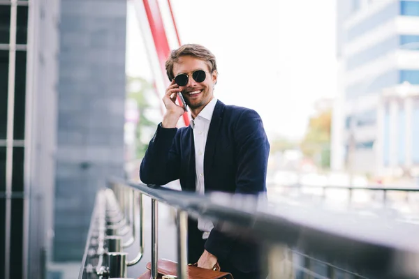 Менеджер в солнечных очках улыбается, разговаривая по мобильному телефону на улице — стоковое фото