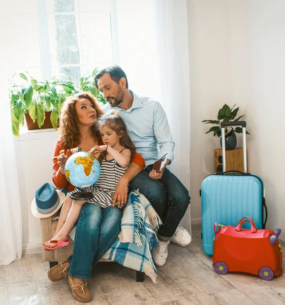 Gelukkige ouders en kleine dochter zitten aan fauteuil studeren wereldbol. — Stockfoto