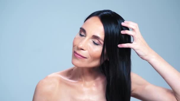 Красивая брюнетка с голыми плечами прибирает волосы, позируя перед камерой — стоковое видео