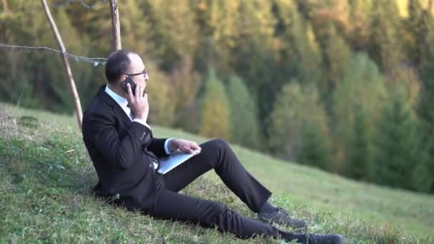 Empresario en gafas está sentado en la hierba — Vídeos de Stock