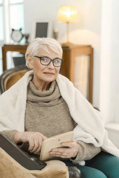 Sonriente dama de pelo gris sosteniendo su tableta y mirando a la cámara — Foto de Stock