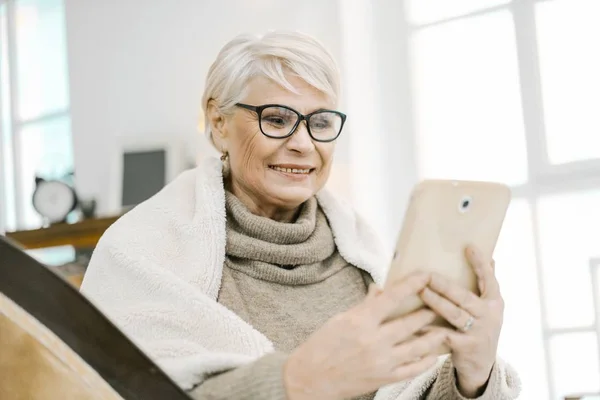 Wanita berambut abu-abu tua membaca sesuatu yang menyenangkan di Tabletnya dan tersenyum — Stok Foto