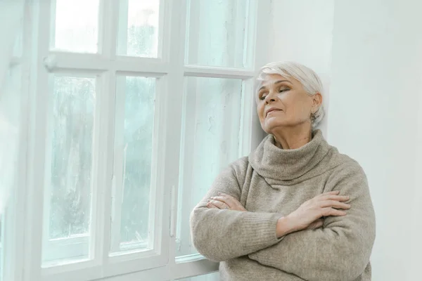 Bedachtzame oudere vrouw die naar het raam kijkt — Stockfoto