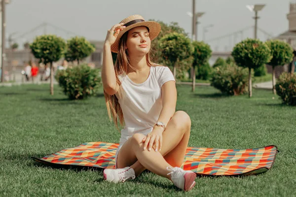 Девушка сидит на одеяле на траве в парке со скрещенными ногами . — стоковое фото