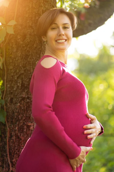 Mulher grávida bonita sorri na natureza no dia ensolarado — Fotografia de Stock