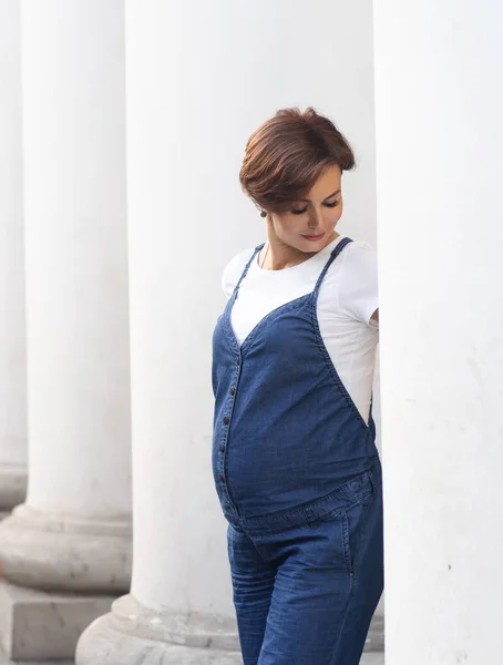 Stijlvolle zwangere vrouw poseert onder witte zuilen — Stockfoto