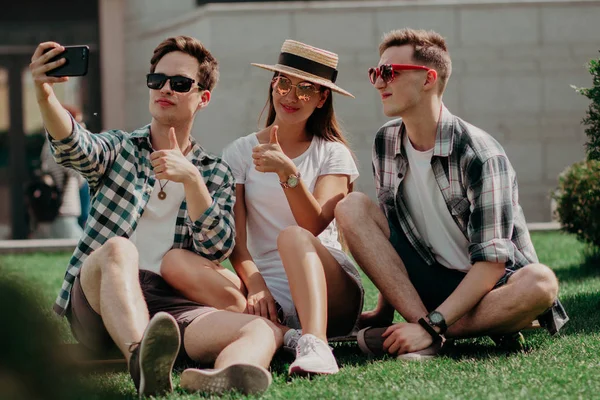 Um grupo de jovens amigos selfies fazendo um polegar no gramado ensolarado — Fotografia de Stock