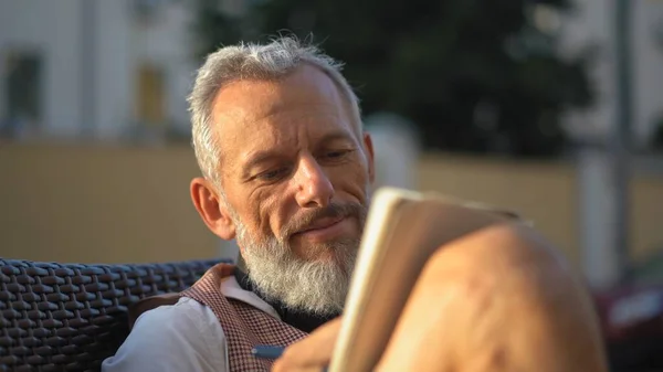 Grey bearded man happily writes down ideas in a notebook on his knees — Stock Photo, Image