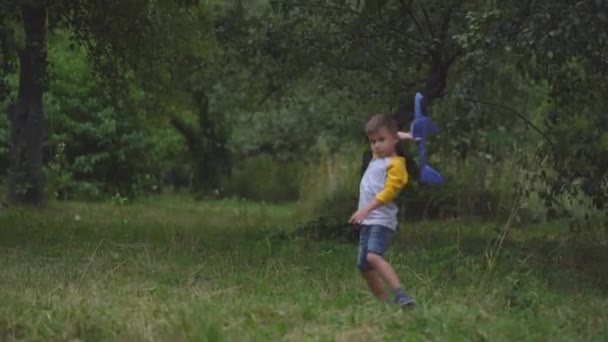 Een kleine jongen die met een blauw speelgoedvliegtuig vliegt — Stockvideo