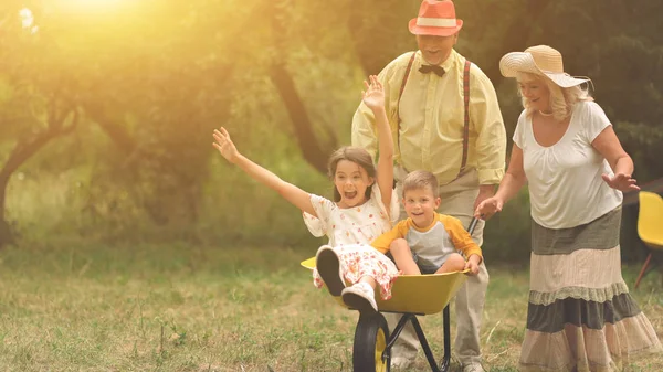 Grandma And Grandpa Are Pushing Their Grandchildren In A Wheelbarrow — Stok fotoğraf