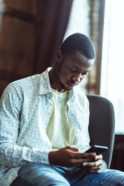 Mladý černošky chlap chatuje v telefonu sedí v útulné kanceláři — Stock fotografie