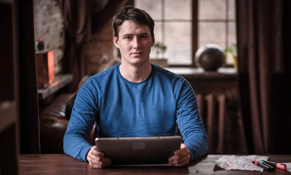 Serious Young Man utiliza su tableta mientras trabaja en un acogedor espacio de coworking . — Foto de Stock