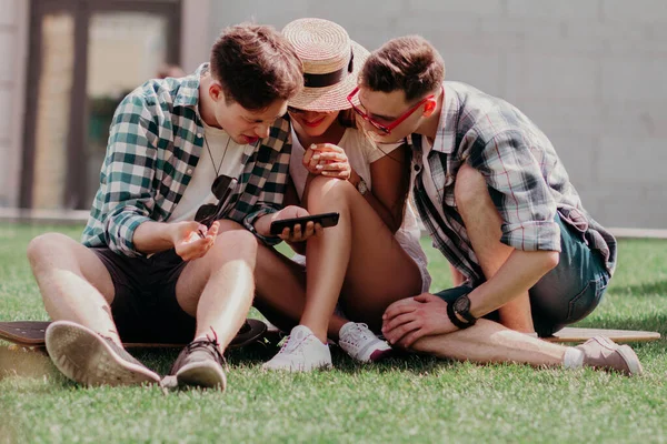 Tre ragazzi piegati insieme guardando il telefono sull'erba . — Foto Stock