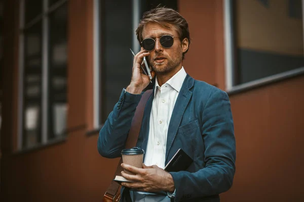 Handsome young businessman holding disposable cup and talking on the phone — Stock fotografie