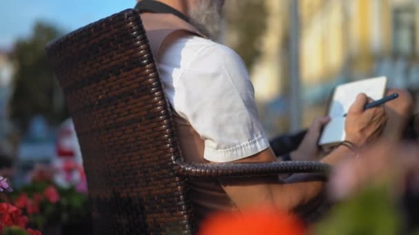 Schizzi dello scrittore grigio nel taccuino nel caffè di strada — Video Stock