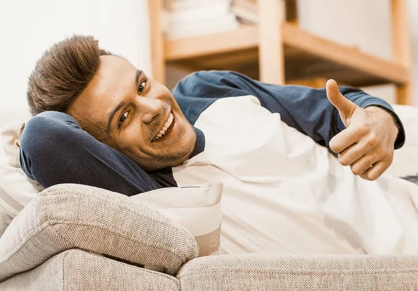 Χαμογελώντας άνδρες δείχνει εντάξει χειρονομίες ξαπλωμένη στον καναπέ — Φωτογραφία Αρχείου