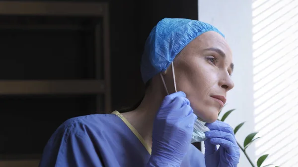 Mulheres cansadas Medic olha para a janela tirando máscara — Fotografia de Stock